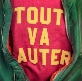 Photography. close up. Opened green MA1 on red sweat with yellow print on front. Tout va sauter. 