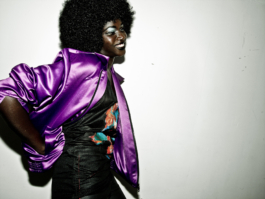 Photography. Model wears a purple silk jacket and black printed top. Night club. 