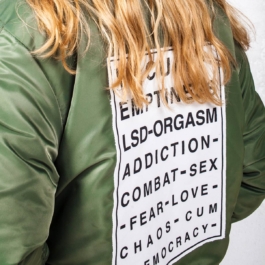 Photography. Fashion editorial. Close up. Blond model wearing a MA1 jacket with vision test printed on back. 